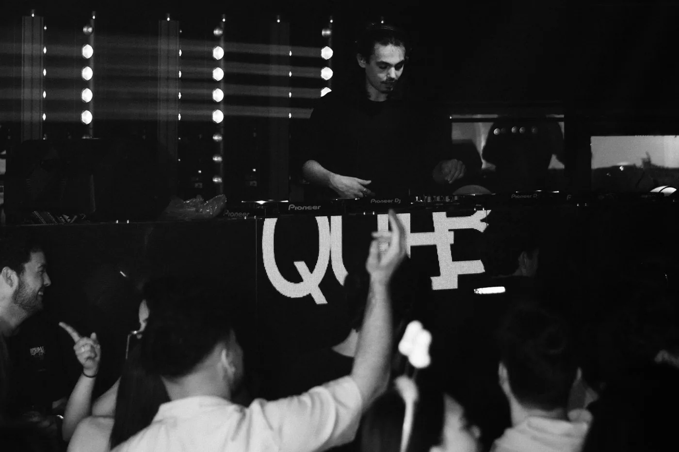 Fotografía en blanco y negro de un DJ en cabina con el público bailando delante